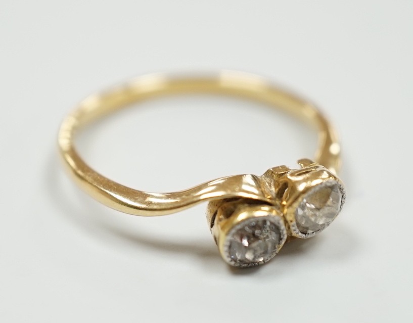 A yellow metal and collet set two stone diamond cross over ring, size L, gross weight 1.9 grams.